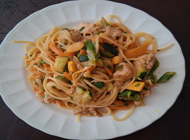A colorful plate of pork pasta with green and yellow zucchini, broccoli, carrots, green beans, and green onions, garnished with black pepper, showcasing a vibrant and hearty home-cooked meal.